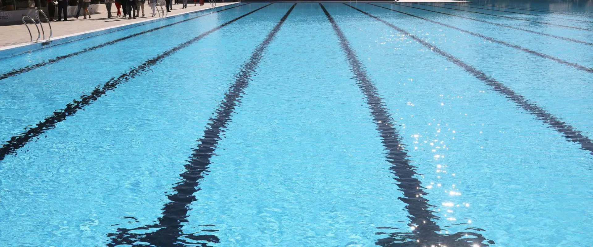 Piscina de verano de un centro deportivo municipal de Madrid, con calles marcadas y árboles al fondo